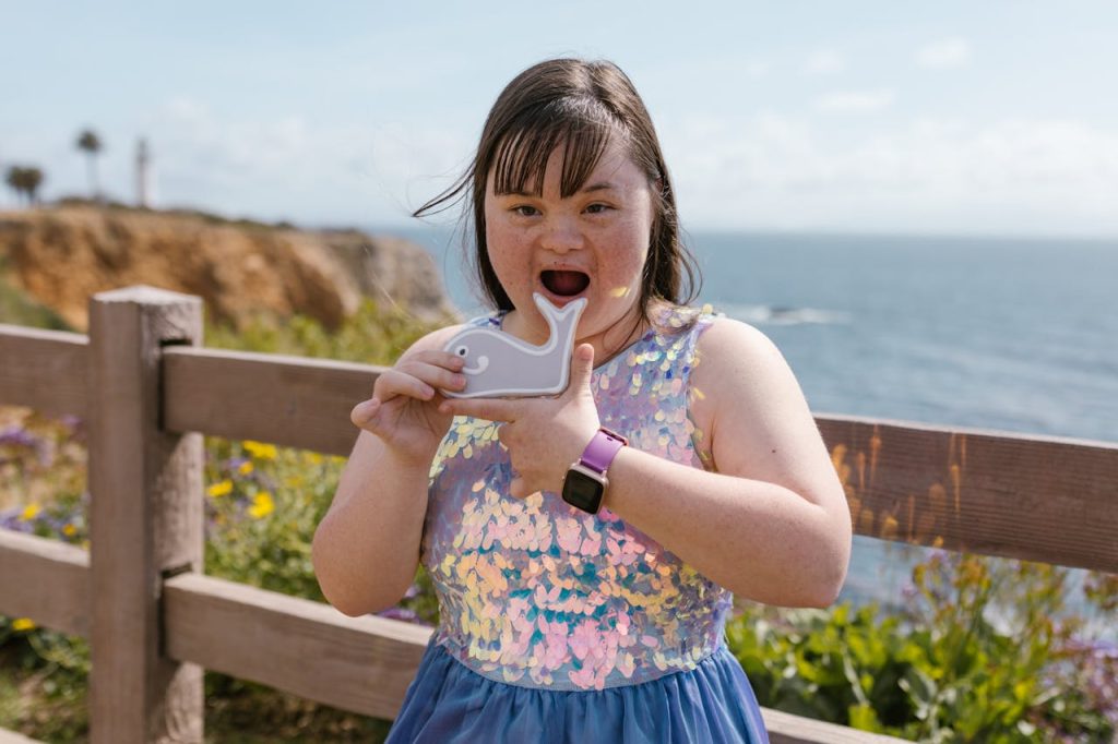 a-girl-holding-a-whale-shaped-cookie-7403189 A joyful girl with Down Syndrome holding a whale toy by the sea.